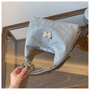 Detailed view of silver butterfly ornament on pleated metallic grey shoulder bag