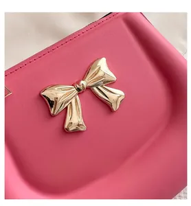 Close-up of peach pink saddle bag featuring a decorative golden metal bow clasp