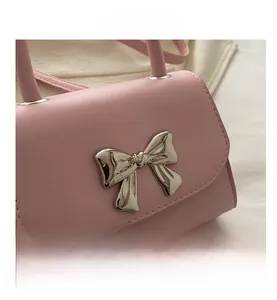 Detailed view of pink leather handbag featuring a glossy silver metal bow and fine stitching