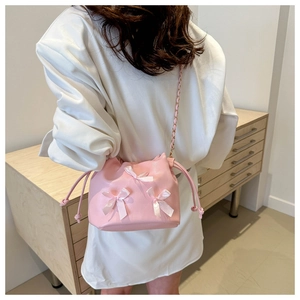 Detail of pink drawstring bucket bag with white satin bows and gold chain strap