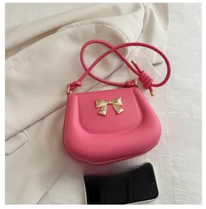 Pink saddle shoulder bag with golden bow and smartphone for size comparison reference