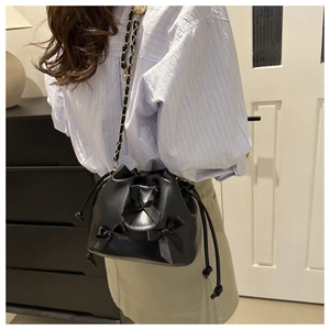 Detail of black drawstring bucket bag featuring elegant ribbon bows and gold chain strap