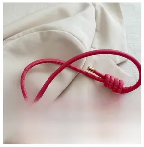Detail of pink handbag with knotted tubular strap and gold metal tips on white blazer