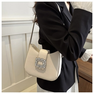 Detail of elegant cream leather handbag with sparkling crystal square buckle on black coat