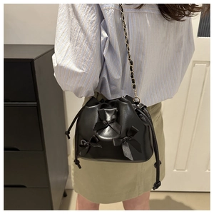 Detail of black drawstring bucket bag featuring sweet bows and metal chain strap