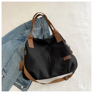Detail einer schwarzen Canvas-Tasche mit braunem Fashion-Label und verstellbarem Gurt