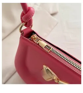 Detail of pink handbag featuring a gold zipper and decorative knot on the handle