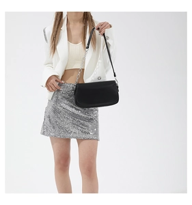 Model wearing a black leather underarm bag with silver chain strap and matte finish
