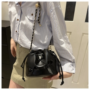 Detail view of black pleated bucket bag with bow accents and gold bead chain strap