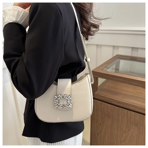 Detail view of cream half-moon underarm bag featuring a signature rhinestone square buckle