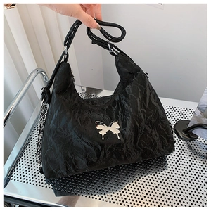 Detail of black pleated crossbody bag with silver butterfly metal ornament and chain