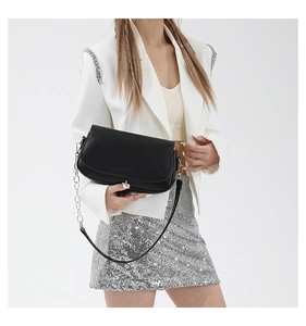 Detail of black leather saddle bag with silver asymmetric buckle and chain strap