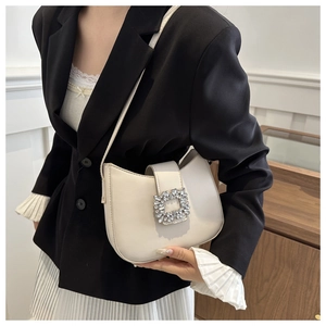Detail of a creamy white leather underarm bag featuring a luxury rhinestone buckle