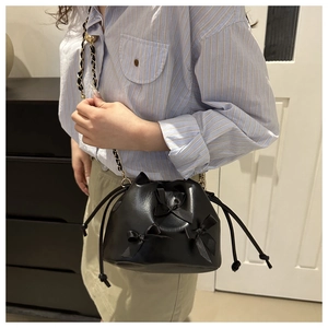 Detail of black drawstring bucket bag with decorative bows and black gold woven chain strap