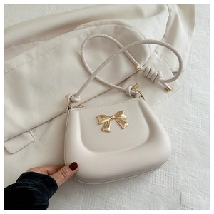 Detail of a creamy beige handbag featuring a gold bow accent and tied shoulder strap