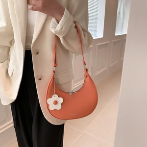 Chic orange half-moon shoulder bag with a white floral charm on a stylish model