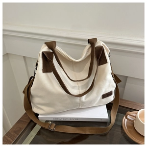 Detail of canvas tote bag featuring brown straps and a leather fashion tag on white books