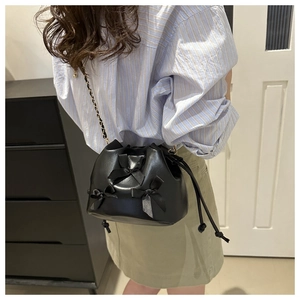 Détail du sac seau noir avec nœuds décoratifs et bandoulière en chaîne dorée