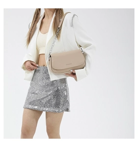 Close-up of nude saddle bag with silver chain strap worn by model in chic outfit