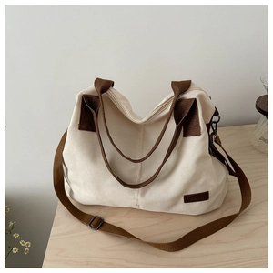 Detailansicht der beigen Canvas-Tasche mit braunen Trägern und Fashion-Logo auf Holz