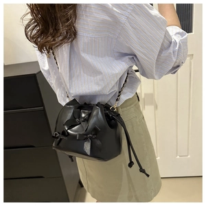Detail of a black leather bucket bag with ribbon bows and golden chain strap