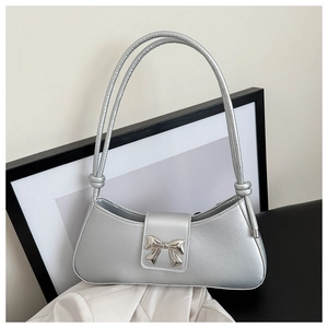 Detail of silver metallic underarm bag featuring a delicate metal bow and textured finish