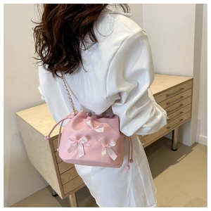 Detail of pink drawstring bucket bag with silk bows and metal chain strap on model