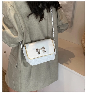 Detailed look at white quilted flap shoulder bag with silver bow buckle and chain strap