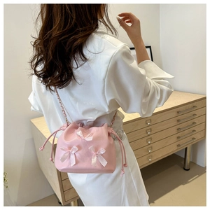 Pink pleated drawstring bucket bag with silk bows and gold-tone chain strap on a model