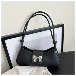 Detail of minimalist black leather shoulder bag featuring a silver metal bow accent