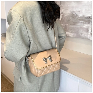 Quilted crossbody bag with metal bow detail and chain strap shown on a model