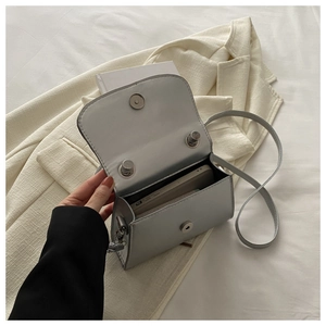Dettaglio di una mini borsa a tracolla minimalista con fibbia metallica magnetica su blazer