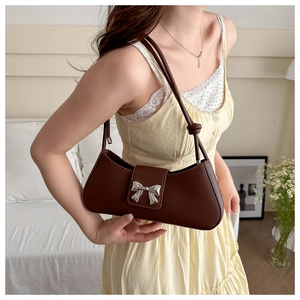 Dettaglio borsa baguette in pelle marrone scuro con fibbia a fiocco e tracolla