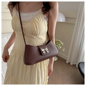 Dettaglio di una borsa baguette in pelle marrone scuro con fiocco in metallo argento