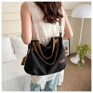 Detail der schwarzen Canvas-Tasche mit Fashion-Etikett, braunen Trägern und Metallhaken
