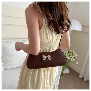 Detail of a dark brown baguette bag with a silver bow clasp on a yellow dress