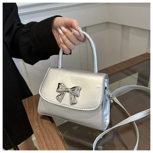 Dettaglio di una mini borsa quadrata argento con fiocco metallico e finitura perlata