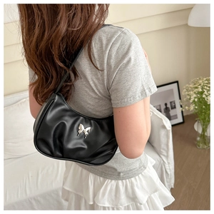 Detail of black glossy crescent bag with silver butterfly buckle worn on shoulder