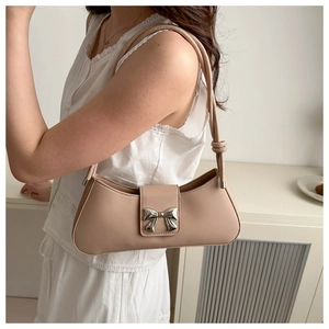 Detail of minimalist beige baguette bag with silver bow clasp and knotted strap detail
