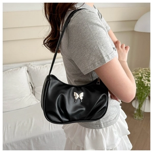 Detail of black pleated crescent bag with silver butterfly charm shown on shoulder