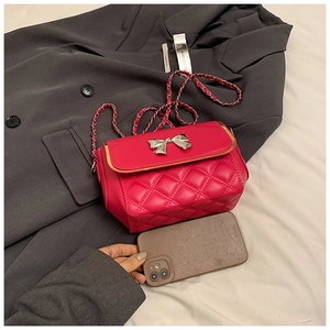 Detailed view of magenta quilted crossbody bag with silver bow buckle next to a phone