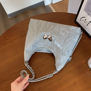 Silver metallic hobo bag with butterfly hardware on a minimalist wooden background