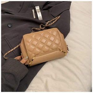 Close-up of beige quilted leather crossbody bag with gold chain strap on grey blazer