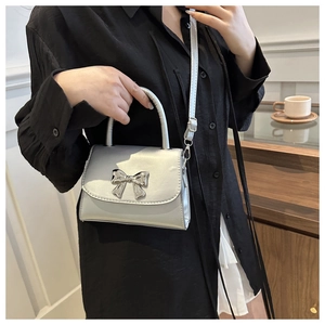 Close-up of a silver mini square bag with a metallic bow clasp shown on a model