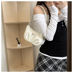 Detail of silver butterfly hardware on a white pleated shoulder bag worn by a model