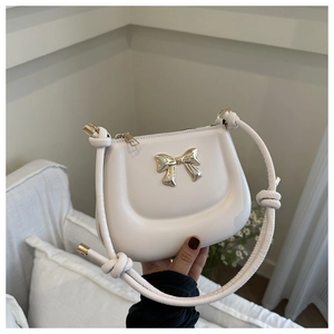 Detail of cream-white saddle bag with golden bow buckle and knotted leather strap