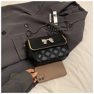 Detail of black quilted crossbody bag featuring silver bow accent and chain strap