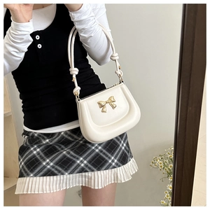 Detail of creamy white faux leather handbag featuring a golden metal bow and knotted strap