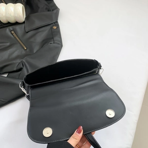 Minimalist matte black PU leather saddle bag with magnetic closures on white fabric background