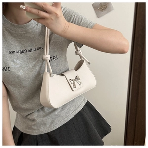 Close-up of cream square underarm bag with silver bow accent and knotted shoulder strap